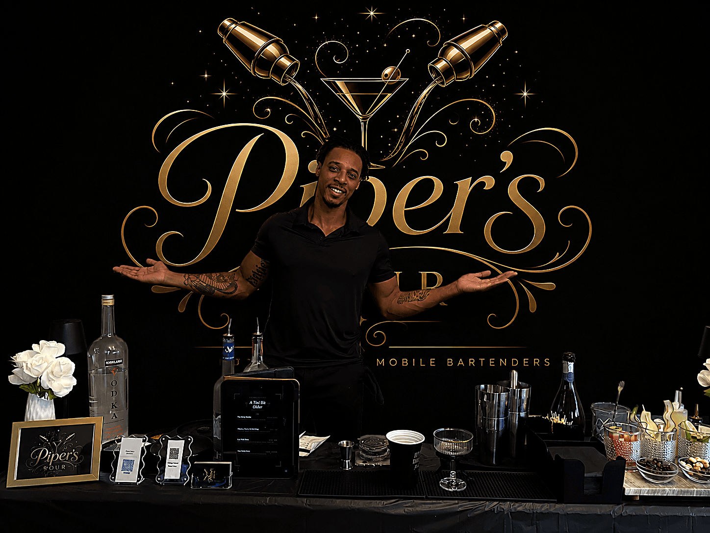 DJ Piper, owner of Piper's Pour, behind his mobile bar setup with the Piper's Pour logo signage